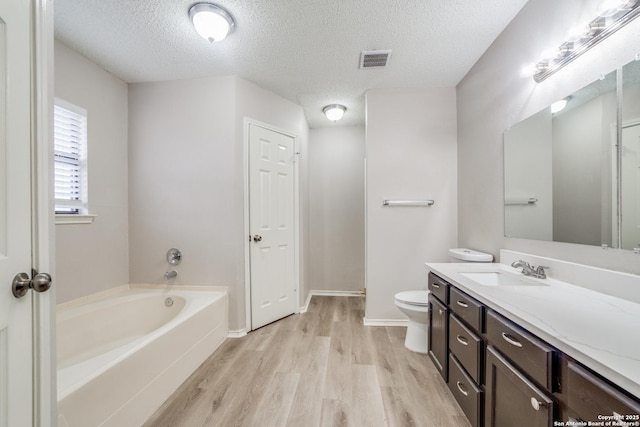 bathroom featuring a textured ceiling, hardwood / wood-style flooring, toilet, a tub to relax in, and vanity