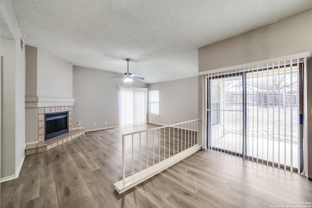 unfurnished living room with hardwood / wood-style floors, a tile fireplace, vaulted ceiling, ceiling fan, and a textured ceiling