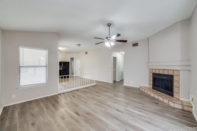 unfurnished living room featuring lofted ceiling, a tile fireplace, ceiling fan, and light hardwood / wood-style flooring