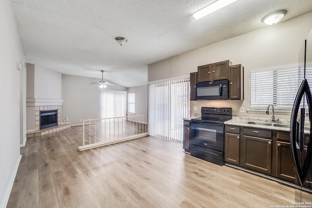 kitchen featuring a tile fireplace, black appliances, sink, dark brown cabinets, and lofted ceiling