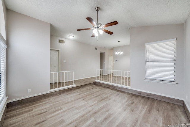 unfurnished room with ceiling fan with notable chandelier, light hardwood / wood-style floors, a textured ceiling, and vaulted ceiling