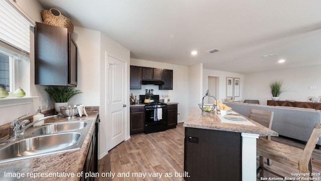 kitchen with light hardwood / wood-style flooring, black gas range oven, a kitchen island with sink, a kitchen breakfast bar, and sink