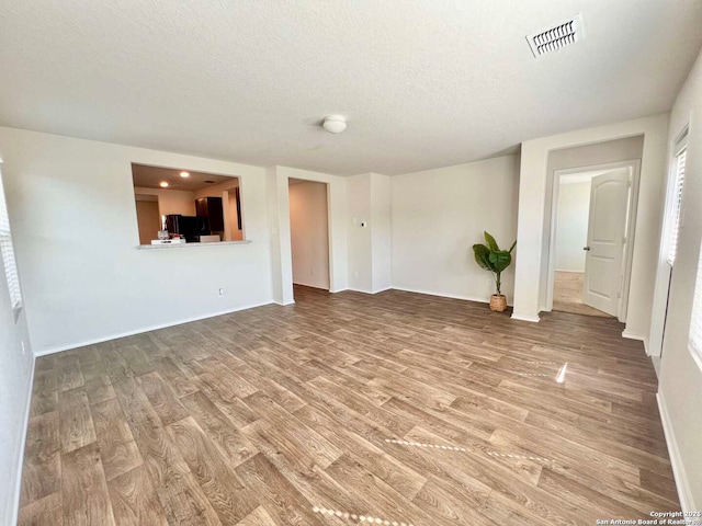 unfurnished living room with a textured ceiling and light hardwood / wood-style flooring