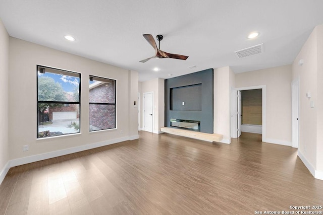 unfurnished living room featuring a large fireplace, hardwood / wood-style flooring, and ceiling fan