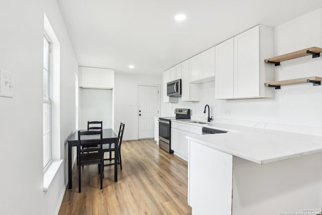 kitchen with kitchen peninsula, stainless steel appliances, light wood-type flooring, white cabinets, and sink