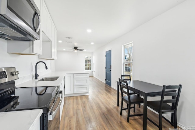 kitchen featuring light hardwood / wood-style floors, white cabinetry, appliances with stainless steel finishes, ceiling fan, and sink