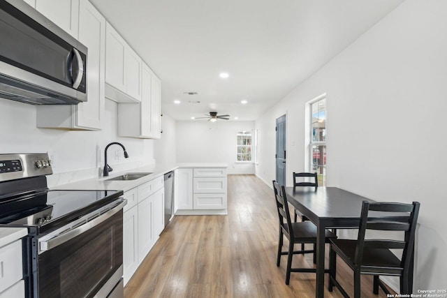 kitchen featuring stainless steel appliances, sink, white cabinets, ceiling fan, and light hardwood / wood-style floors