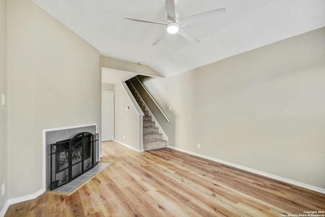 unfurnished living room with light hardwood / wood-style floors, a tiled fireplace, ceiling fan, and vaulted ceiling