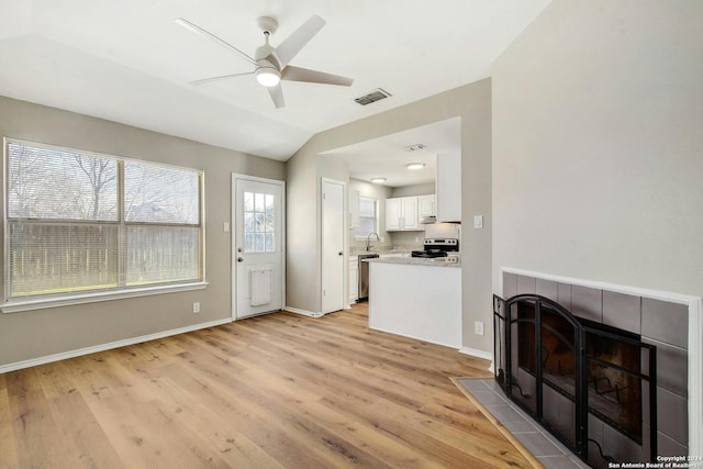 living room with light hardwood / wood-style flooring, lofted ceiling, a tiled fireplace, ceiling fan, and sink