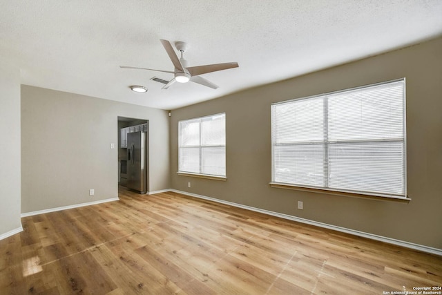 empty room with a textured ceiling, light wood-type flooring, and ceiling fan