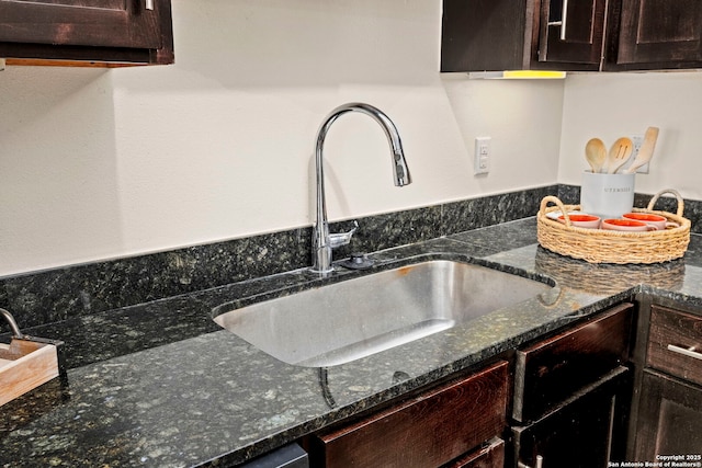 kitchen with sink, dark brown cabinets, and dark stone countertops