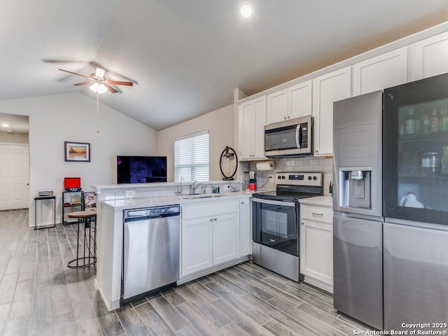 kitchen with sink, white cabinetry, vaulted ceiling, kitchen peninsula, and appliances with stainless steel finishes