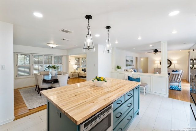 kitchen featuring stainless steel microwave, butcher block counters, hanging light fixtures, a kitchen island, and light hardwood / wood-style flooring