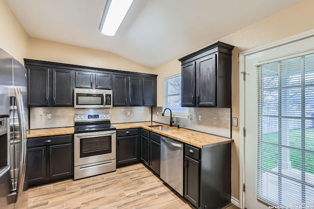 kitchen featuring vaulted ceiling, sink, backsplash, light hardwood / wood-style floors, and stainless steel appliances