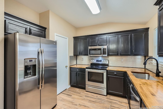 kitchen featuring vaulted ceiling, butcher block counters, sink, backsplash, and stainless steel appliances