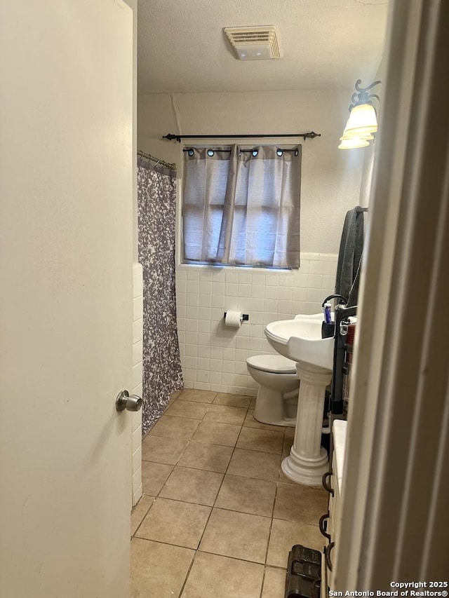 bathroom featuring tile walls, a textured ceiling, toilet, and tile patterned floors