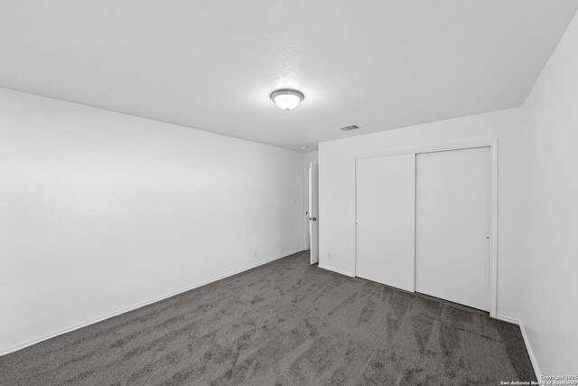 unfurnished bedroom featuring a textured ceiling, dark colored carpet, and a closet