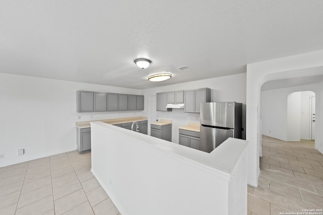 kitchen featuring a textured ceiling, light tile patterned flooring, stainless steel fridge, a kitchen island, and gray cabinetry