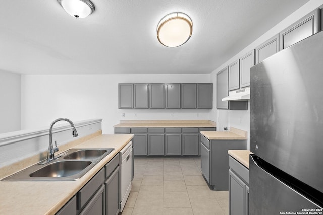 kitchen with sink, light tile patterned floors, white dishwasher, stainless steel refrigerator, and gray cabinets