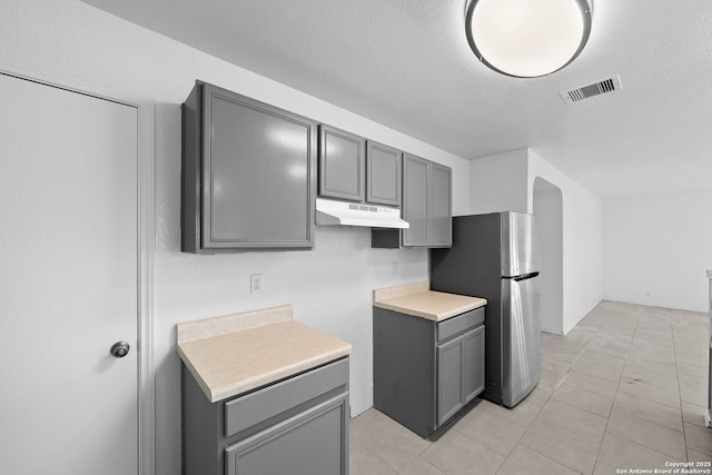 kitchen with a textured ceiling, light tile patterned floors, gray cabinetry, and stainless steel fridge