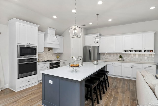 kitchen with stainless steel appliances, white cabinetry, a center island with sink, and custom exhaust hood