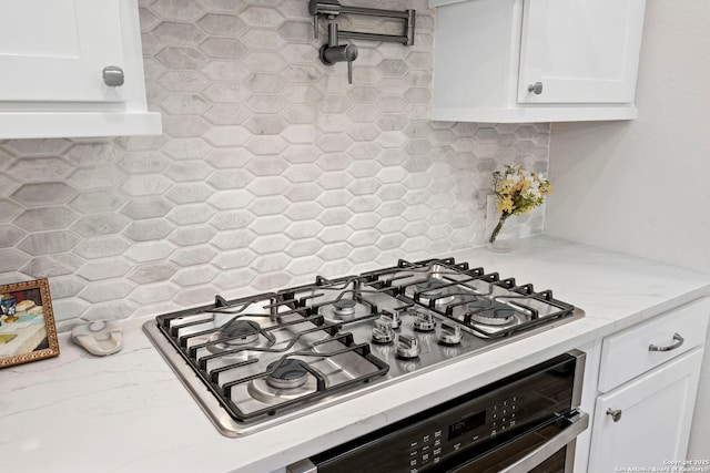 kitchen featuring light stone countertops, appliances with stainless steel finishes, white cabinets, and decorative backsplash