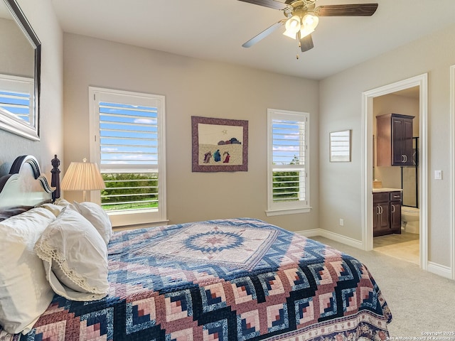 bedroom with ensuite bathroom, light colored carpet, and ceiling fan