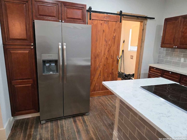 kitchen with dark hardwood / wood-style floors, tasteful backsplash, a barn door, stainless steel fridge with ice dispenser, and stovetop