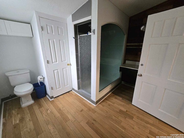 bathroom with vaulted ceiling, toilet, hardwood / wood-style flooring, a textured ceiling, and an enclosed shower