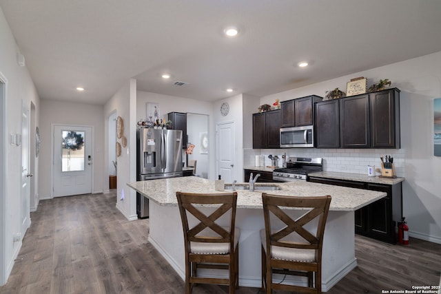 kitchen with dark wood-type flooring, a center island with sink, appliances with stainless steel finishes, and dark brown cabinets