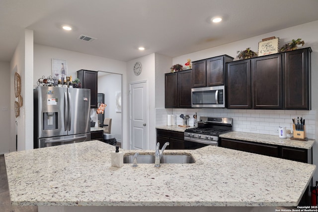 kitchen with sink, stainless steel appliances, an island with sink, and decorative backsplash