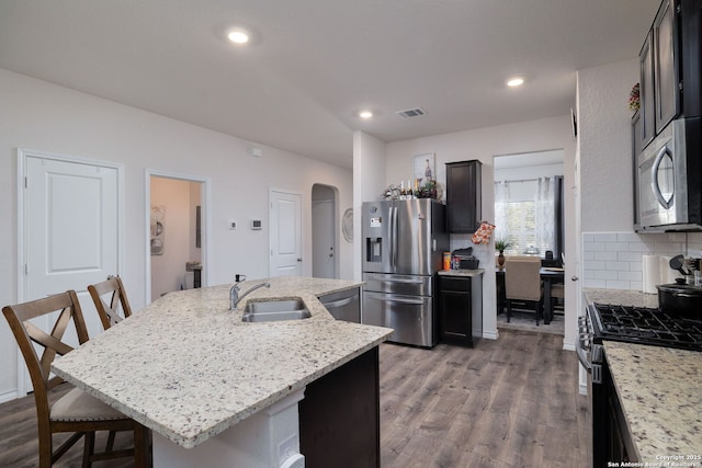 kitchen with sink, a kitchen breakfast bar, light stone countertops, a kitchen island with sink, and appliances with stainless steel finishes