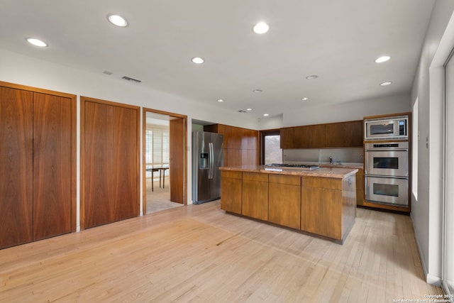 kitchen with appliances with stainless steel finishes, light wood-type flooring, a wealth of natural light, and a kitchen island