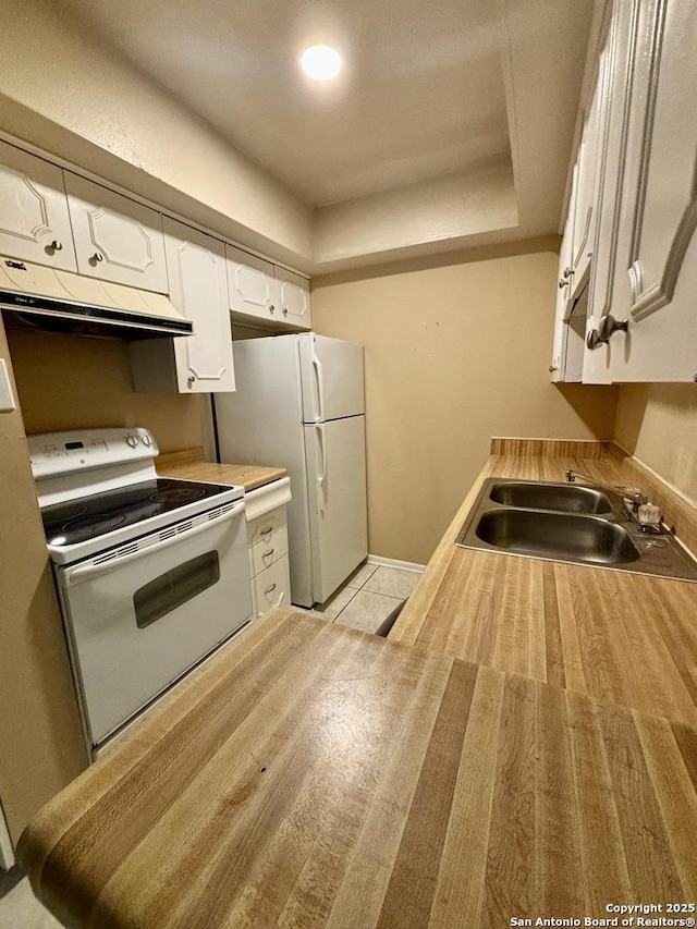 kitchen featuring white appliances, white cabinets, a tray ceiling, and sink