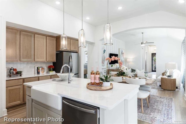 kitchen with a kitchen island with sink, stainless steel appliances, hanging light fixtures, ceiling fan, and tasteful backsplash