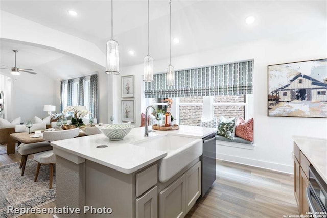 kitchen featuring stainless steel dishwasher, vaulted ceiling, hanging light fixtures, a center island with sink, and sink