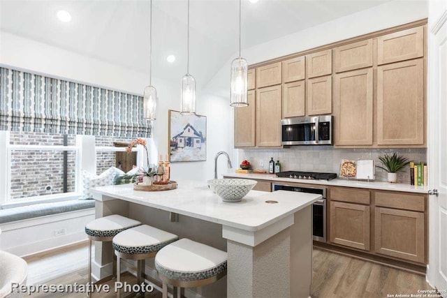 kitchen featuring a kitchen island with sink, stainless steel appliances, light hardwood / wood-style flooring, decorative light fixtures, and tasteful backsplash