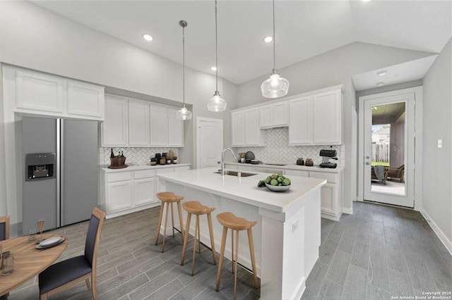 kitchen with hanging light fixtures, stainless steel fridge, a kitchen island with sink, white cabinetry, and sink