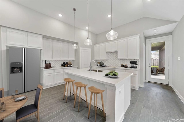 kitchen featuring sink, white cabinets, decorative light fixtures, stainless steel fridge, and a center island with sink