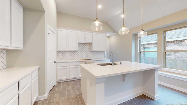 kitchen with decorative backsplash, hanging light fixtures, white cabinetry, and an island with sink