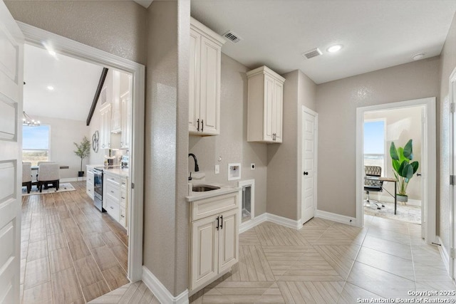 kitchen featuring sink, stainless steel electric range oven, an inviting chandelier, and white cabinets