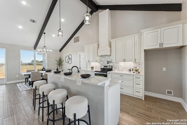 kitchen featuring decorative light fixtures, white cabinets, electric stove, and an island with sink