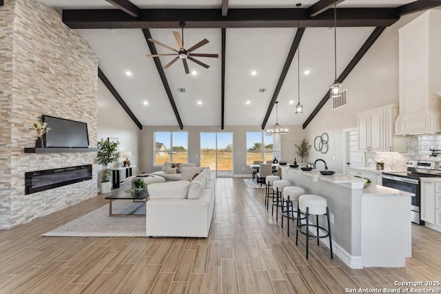 living room with sink, a fireplace, beamed ceiling, ceiling fan with notable chandelier, and high vaulted ceiling