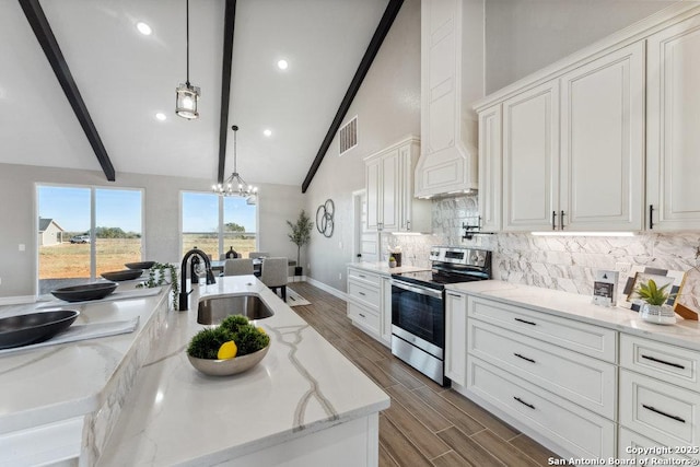 kitchen featuring a center island with sink, hanging light fixtures, light stone countertops, stainless steel range with electric stovetop, and sink