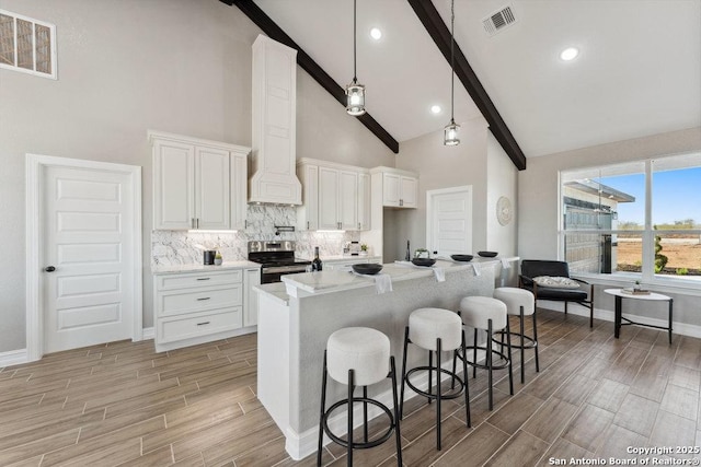 kitchen with white cabinets, a kitchen bar, stainless steel electric range, a center island with sink, and high vaulted ceiling