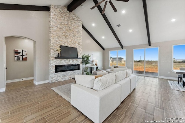 living room with high vaulted ceiling, ceiling fan, beam ceiling, and a stone fireplace