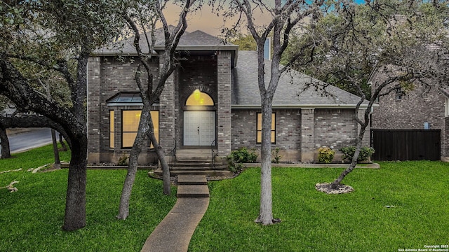 view of front of house featuring brick siding, a front lawn, a shingled roof, and fence