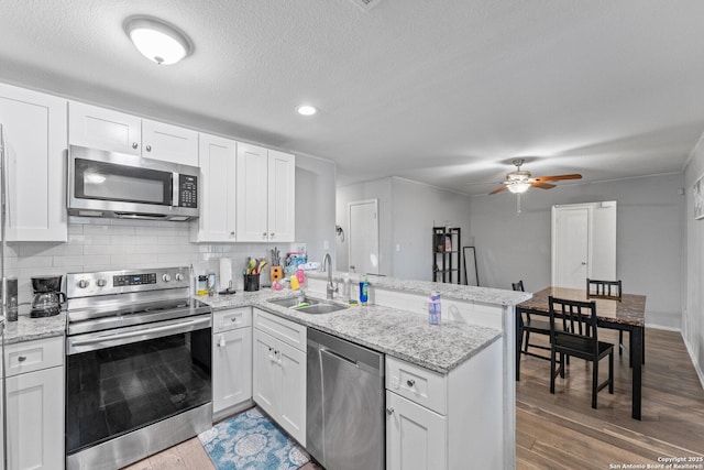 kitchen featuring wood-type flooring, stainless steel appliances, kitchen peninsula, sink, and white cabinetry