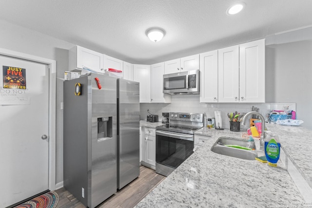 kitchen featuring stainless steel appliances, sink, white cabinetry, tasteful backsplash, and light stone countertops