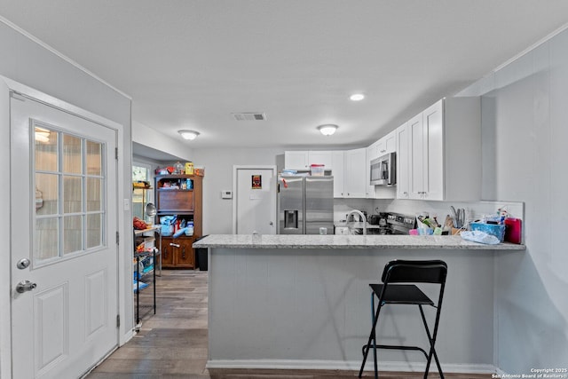 kitchen with kitchen peninsula, white cabinets, light wood-type flooring, and appliances with stainless steel finishes